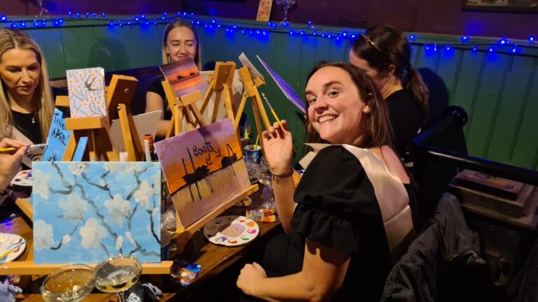 A woman poses for a photo while participating in Paint and Prosecco, a group activity for hen parties, weddings, and birthday parties.